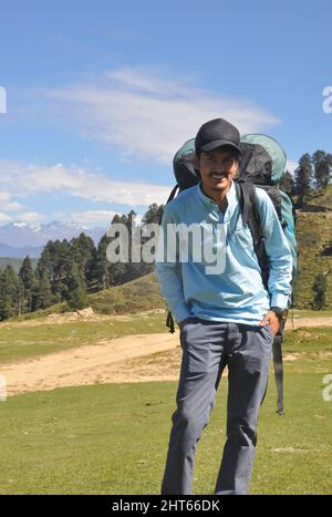 Vorderansicht eines glücklichen jungen Mannes mit Mütze und Fallschirmrucksack im Berg Stockfoto
