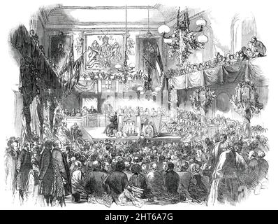 The Cardiff Athenaeum Eisteddfod, 1850. Walisisches Kulturereignis: "Der Saal wurde zu diesem Anlass mit den Flaggen der Schiffe im Hafen dekoriert ... und eine Fülle von Evergreens, hauptsächlich Lorbeer, wurden im Raum aufgestellt...auf dem zentralen Lampenstiel wurde ein Haufen Lauch, symbolisch für das Fürstentum, geschmackvoll eingerichtet. Vor dem Vorsitzenden und anderen Richtern der Vorstellung war ein großer Tisch, der mit mechanischen Gegenständen bedeckt war - wie Uhren, unter Glasschirmen; ein Modell einer Kohlenschiffsbühne; ein Transitinstrument, &amp;c. Die Preisharfe besetzte das rechte Ende des Tisches.“ Harpis Stockfoto