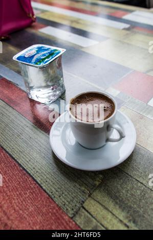 Reicher und hochkoffeinierter türkischer Kaffee in traditioneller Tasse und eine Plastikschale Wasser auf einem Tisch Stockfoto