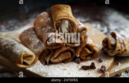 Zusammengerollte Pfannkuchen mit Quark und Rosinen auf Holzständer mit Mehl. Selektiver Fokus Stockfoto