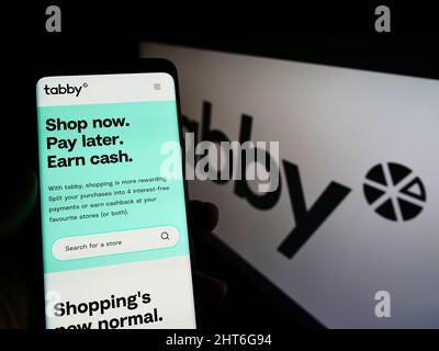 Person, die Mobiltelefon mit der Website der arabischen Finanzgesellschaft Tabby FZ LLC auf dem Bildschirm vor dem Logo hält. Konzentrieren Sie sich auf die Mitte des Telefondisplays. Stockfoto