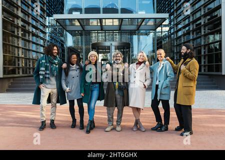 Eine Gruppe von modernen Geschäftsleuten und Frauen vor dem Gebäude, die fröhlich posieren und sich gut Vergnügen Stockfoto