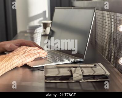 Mann Hände Nahaufnahme tippen auf Laptop-Tastatur. Bisinessman, Freiberufler oder Student, der am Kaffeetisch mit Notizbuch und Takeaway-Tasse sitzt und arbeitet oder studiert. Lifestyle-Konzept der Stadt. Hochwertige Fotos Stockfoto