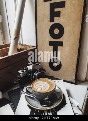 Vertikale Aufnahme einer Tasse Kaffee und einer Vintage-Kamera auf Büchern und Zeitschriften auf einer Fensterbank Stockfoto