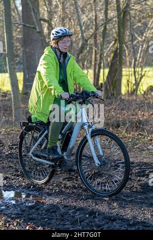 Frau über fünfzig macht mit ihrem E-Bike eine Radtour auf einem schlammigen Weg und durch Pfützen, Lüneburg, Niedersachsen, Deutschland Stockfoto