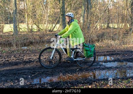 Frau über fünfzig macht mit ihrem E-Bike eine Radtour auf einem schlammigen Weg und durch Pfützen, Lüneburg, Niedersachsen, Deutschland Stockfoto