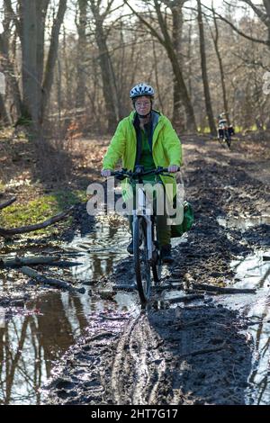 Frau über fünfzig macht mit ihrem E-Bike eine Radtour auf einem schlammigen Weg und durch Pfützen, Lüneburg, Niedersachsen, Deutschland Stockfoto