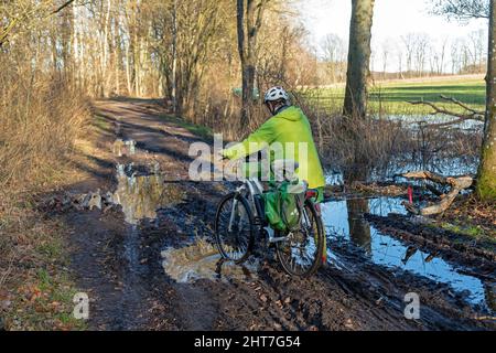 Frau über fünfzig macht mit ihrem E-Bike eine Radtour auf einem schlammigen Weg und durch Pfützen, Lüneburg, Niedersachsen, Deutschland Stockfoto