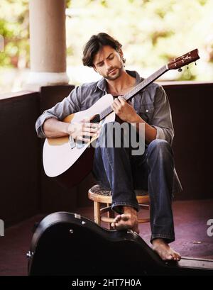 Er weiß genau, welche Akkorde er spielen soll. Hübscher junger Mann, der sitzt und Gitarre spielt. Stockfoto
