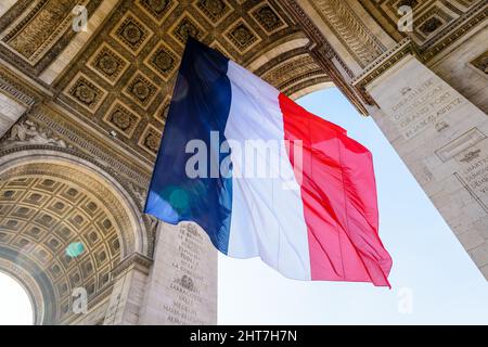 Niedrige Ansicht einer großen französischen Flagge, die unter dem Gewölbe des Triumphbogens in Paris, Frankreich, im Wind flattert. Stockfoto