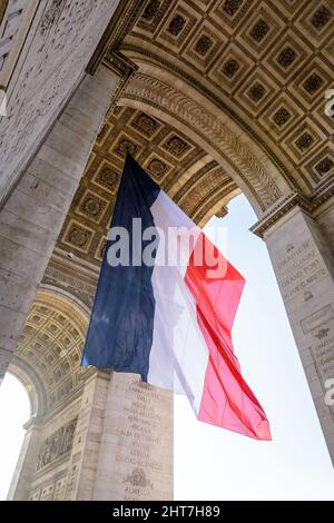 Niedrige Ansicht einer großen französischen Flagge, die unter dem Gewölbe des Triumphbogens in Paris, Frankreich, im Wind flattert. Stockfoto