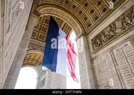 Niedrige Ansicht einer großen französischen Flagge, die unter dem Gewölbe des Triumphbogens in Paris, Frankreich, im Wind flattert. Stockfoto