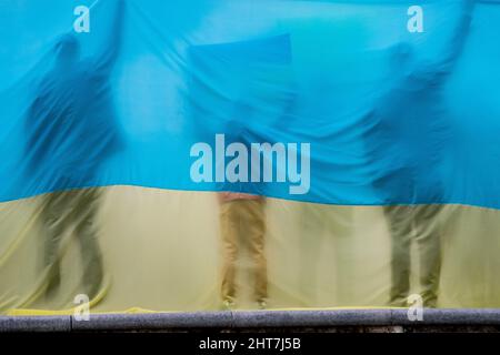 Madrid, Spanien. 27.. Februar 2022. Bei einer Demonstration gegen die russische Invasion in die Ukraine werden durch eine ukrainische Flagge Silhouetten von Menschen gesehen. In Madrid lebende Ukrainer und spanische Unterstützer (mehr als 12,000 laut Polizeibeamten) marschierten durch die Stadt und forderten das Ende des Krieges in der Ukraine und protestierten gegen den russischen Präsidenten Wladimir Putin. Quelle: Marcos del Mazo/Alamy Live News Stockfoto