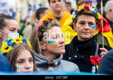 Madrid, Spanien. 27.. Februar 2022. Während einer Demonstration gegen die russische Invasion in die Ukraine werden Demonstranten mit Fahnen auf ihren Gesichtern gesehen. In Madrid lebende Ukrainer und spanische Unterstützer (mehr als 12,000 laut Polizeibeamten) marschierten durch die Stadt und forderten das Ende des Krieges in der Ukraine und protestierten gegen den russischen Präsidenten Wladimir Putin. Quelle: Marcos del Mazo/Alamy Live News Stockfoto