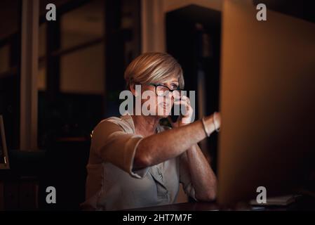 Ich schaue mir gerade die Infos an. Eine kurze Aufnahme einer attraktiven, reifen Geschäftsfrau, die am Computer arbeitet und spät im Büro telefonische Anrufe macht Stockfoto
