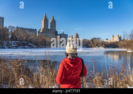 Frau im Central Park im eiskalten Winter mit Blick auf die wunderschöne Aussicht auf das historische Gebäude von New York City im oberen Westen. Stockfoto