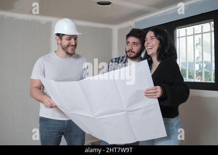 Architekt zeigt dem interessierten glücklichen Paar Baupläne für eine Wohnung. Stockfoto
