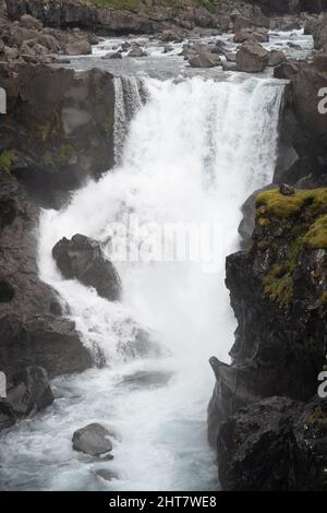 Vertikale Aufnahme eines schäumenden Wasserfalls, der über die schwarzen moosigen Felsen gleitet Stockfoto