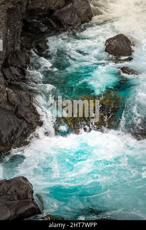 Vertikale Aufnahme eines schäumenden Wasserfalls, der mit hoher Geschwindigkeit die schwarzen, moosigen Felsen hinuntergleitet Stockfoto