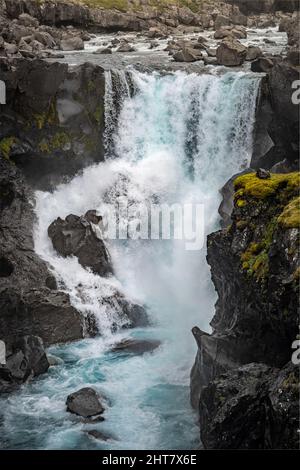 Vertikale Aufnahme eines schäumenden Wasserfalls, der über die schwarzen moosigen Felsen gleitet Stockfoto