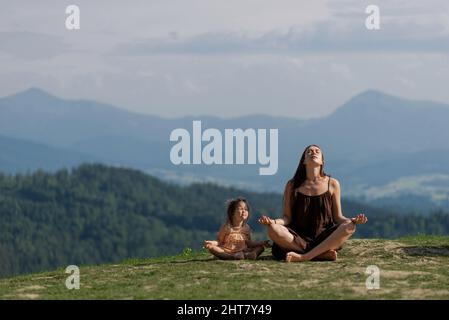 Mutter in Lotuspose in den Bergen mit einer kleinen Tochter, die meditiert Stockfoto