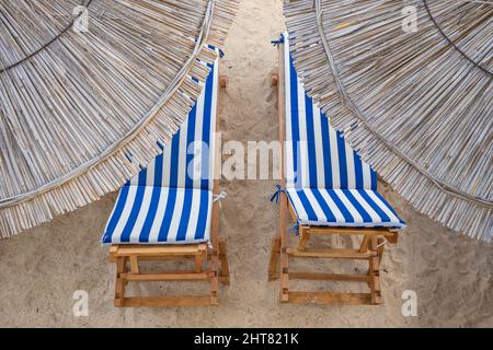 Stroh-Sonnenschirme und zwei Sonnenliegen am leeren Strand aus nächster Nähe Stockfoto