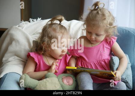 Zwillinge sitzen auf einem Stuhl und schauen sich ein Buch an Stockfoto