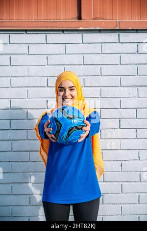 Lächelnde arabische Frau, die mit Ball die Hände ausstreckt Stockfoto