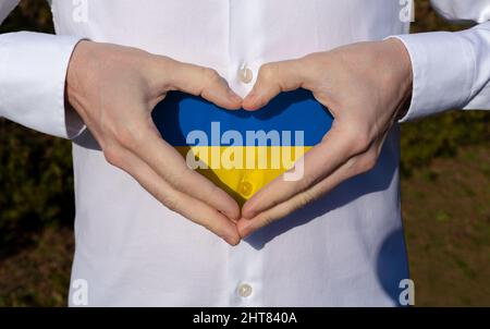 Mann Urlaub seine Hände in herzförmigen auf weißem Hemd mit ukraine-Flagge Farben Unterstützung Konzept . Stockfoto