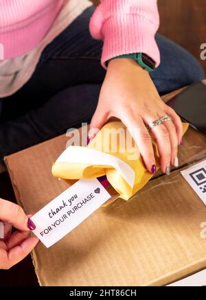 Hoher Winkel der Ernte anonyme weibliche Absender Verpackungsauftrag im Umschlag und Putting Note vielen Dank für den Kauf vor dem Versand in der Box Stockfoto