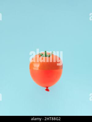 Kreatives Konzept der halben Tomate auf der einen Seite und des roten Ballons auf der anderen. Frisches, saftiges Gemüse auf pastellblauem Hintergrund. Stockfoto