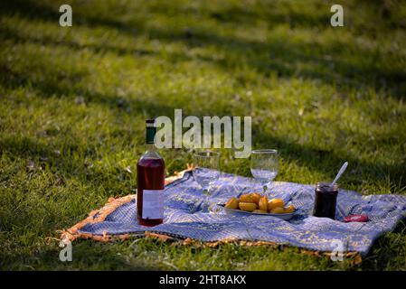 Eine Nahaufnahme von Gläsern Rotwein und Donuts mit Marmelade auf dem grünen Gras während eines romantischen Picknicks Stockfoto