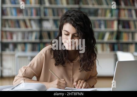 Glückliche junge hispanische Frau, die in der Bibliothek studiert. Stockfoto