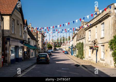 Ein Pfau überquert die Straße vor den traditionellen Geschäften und Häusern der Corsham High Street in Wiltshire, England. Stockfoto