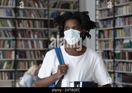 Nachdenkliche junge afroamerikanische männliche Studentin im Facemask schaut weg. Stockfoto