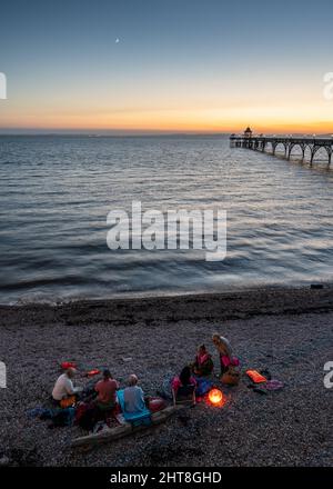 Am Clevedon Beach in Somerset, mit dem Clevedon Pier und dem Bristol Channel dahinter, treffen sich Schwimmer bei Sonnenuntergang. Stockfoto