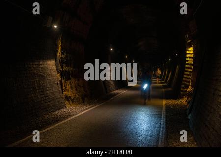 Im dunklen Combe Down Tunnel, Teil der beiden Tunnel Greenway Rail Trail in Bath, Somerset, leuchtet ein Radfahrerscheinwerfer. Stockfoto