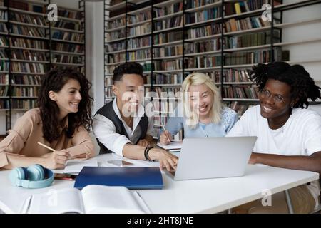 Glückliche junge multiethnische Studenten, die an einem Online-Projekt arbeiten. Stockfoto