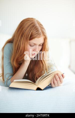 Ihre Nase steckt immer in einem Buch. Ein junges Mädchen liest ihr Buch, während es auf ihrem Bett liegt. Stockfoto