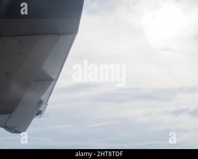 Ein Fragment des Flügels eines fliegenden Flugzeugs vor dem Hintergrund des wolkigen Himmels und der Sonne, die durch den Dunst guckt. Blick vom Bullauge Stockfoto