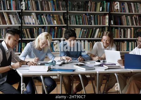 Fokussierte Gruppe von glücklichen, vielfältigen Studenten, die in der Bibliothek studieren. Stockfoto