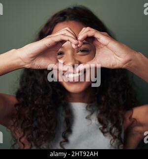 Ein volles Herz ist ein glückliches Herz. Studioaufnahme einer jungen Frau, die eine herzförmige Geste vor grünem Hintergrund macht. Stockfoto