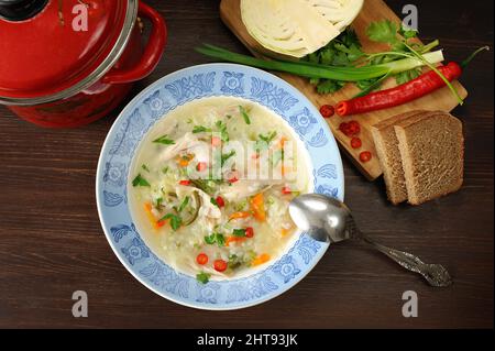Kohlsuppe mit Huhn auf blauem Teller serviert mit Roggenbrot, Chili, frischen Zwiebeln und Kohl Blick über den Kopf Stockfoto