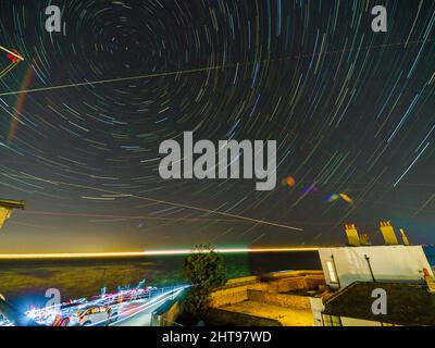 Sheerness, Kent, Großbritannien. 27.. Februar 2022. UK Wetter: Sternentouren zeigen die Rotation der Erde an einem klaren, aber kalten Abend über Sheerness in Kent. Bild: Blick nach Norden in Richtung Polaris - 'der Nordstern' - um den sich die Sterne zu drehen scheinen. Helles Licht am Horizont war ein Kreuzschiff. Fischer & Radwege unten. Gerade Linien sind flache Wege. (Langzeitbelichtung, kamerainterne Komposit von ca. 45 Minuten). Kredit: James Bell/Alamy Live Nachrichten Stockfoto