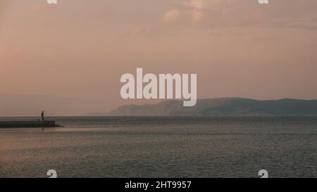 Allein Fischer stehen auf dem Dock und Angeln, Insel Krk im Hintergrund Stockfoto