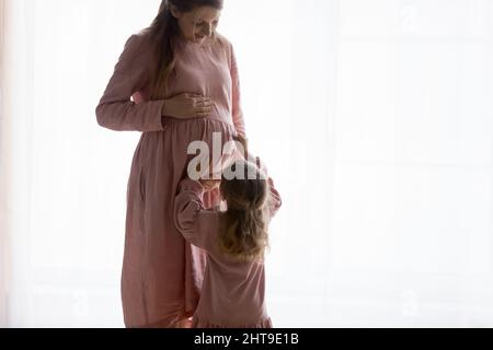 Kleine Tochter Kind trägt natürliche rosa Kleid, berühren schwanger Mutter Stockfoto