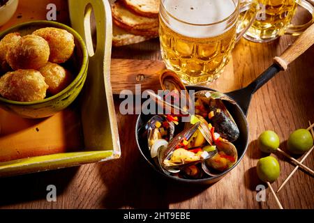 Schüssel mit leckeren Muscheln serviert auf Holztisch mit einem Glas Lagerbier und grünen Oliven Stockfoto