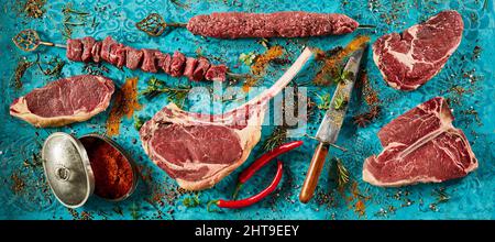 Ein Schuss schmackhafter gegrillter Fleischsteaks und würziger Saucen auf einem blauen Tisch mit frischen Tomaten Stockfoto