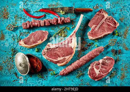 Ein Schuss schmackhafter gegrillter Fleischsteaks und würziger Saucen auf einem blauen Tisch mit frischen Tomaten Stockfoto