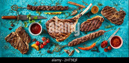 Ein Schuss schmackhafter gegrillter Fleischsteaks und würziger Saucen auf einem blauen Tisch mit frischen Tomaten Stockfoto